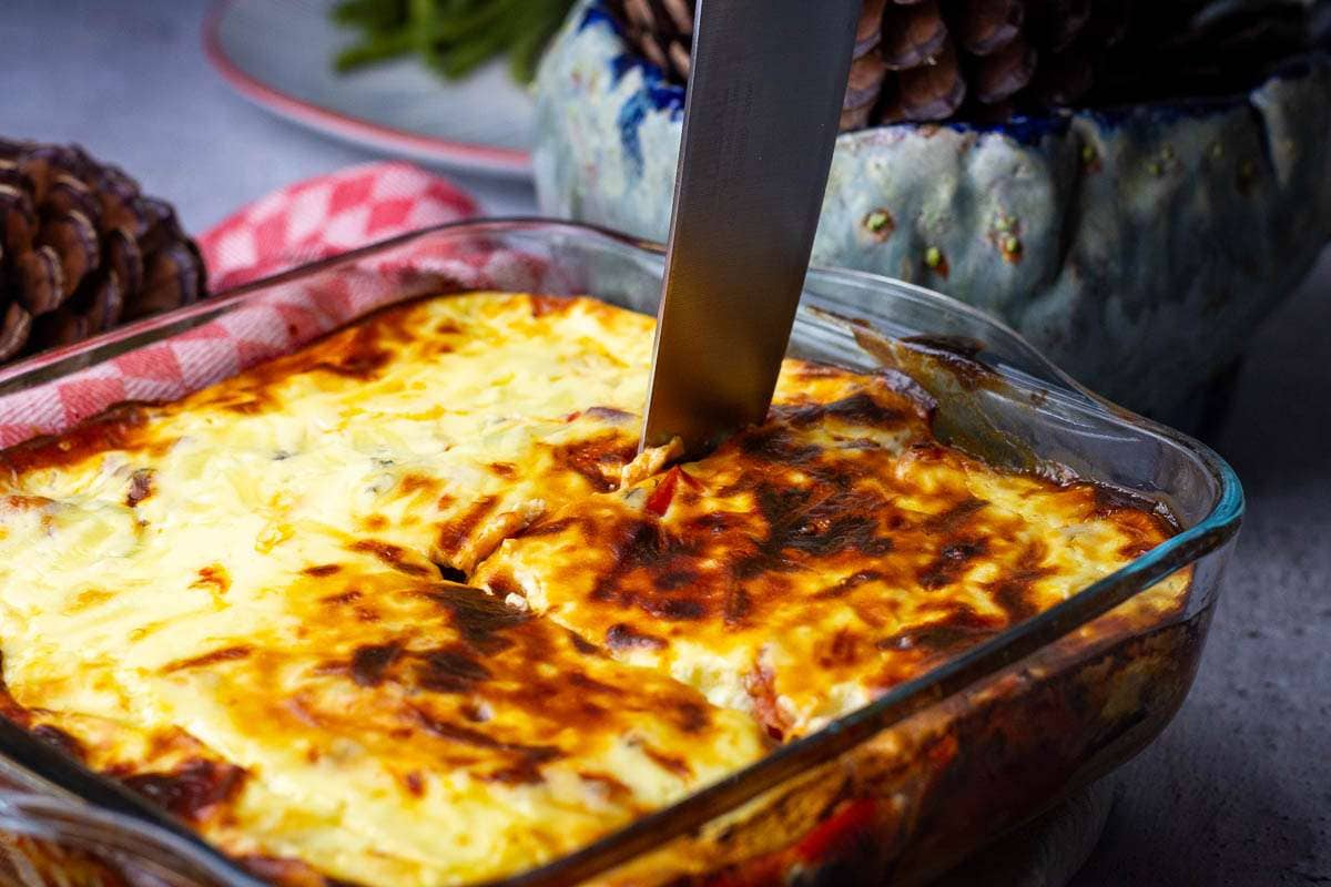 Aubergine bake is being sliced with a large knife.