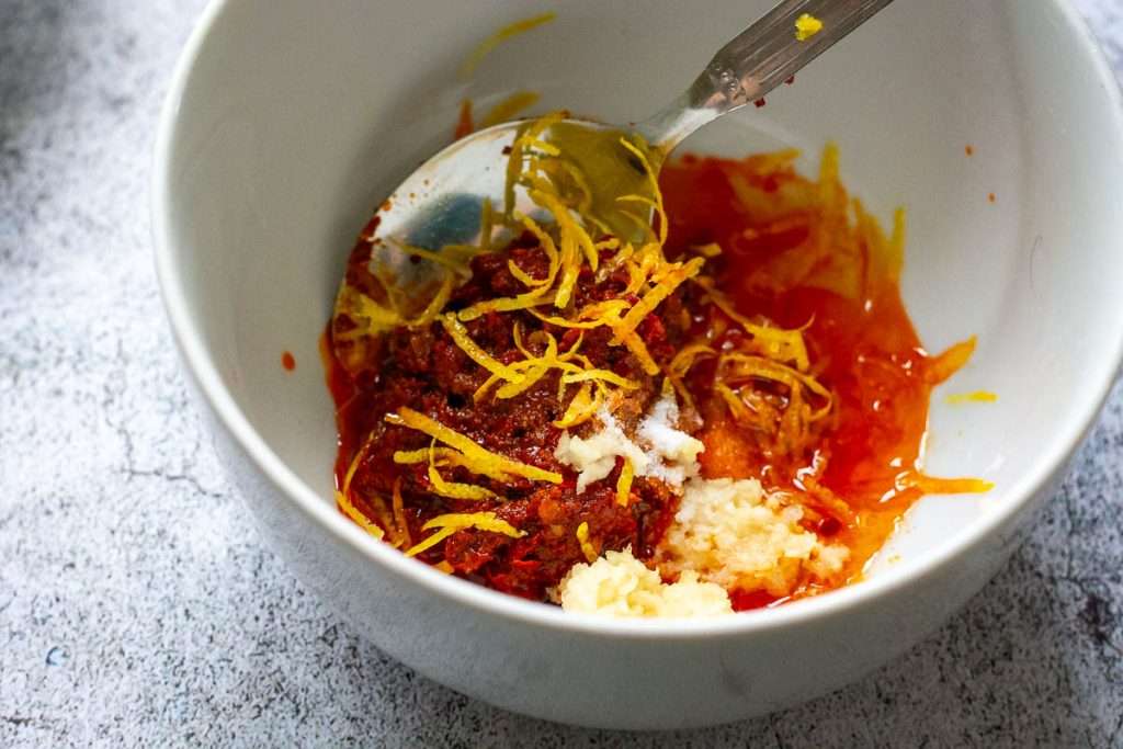 Ingredients for a harissa marinade in a small white bowl.