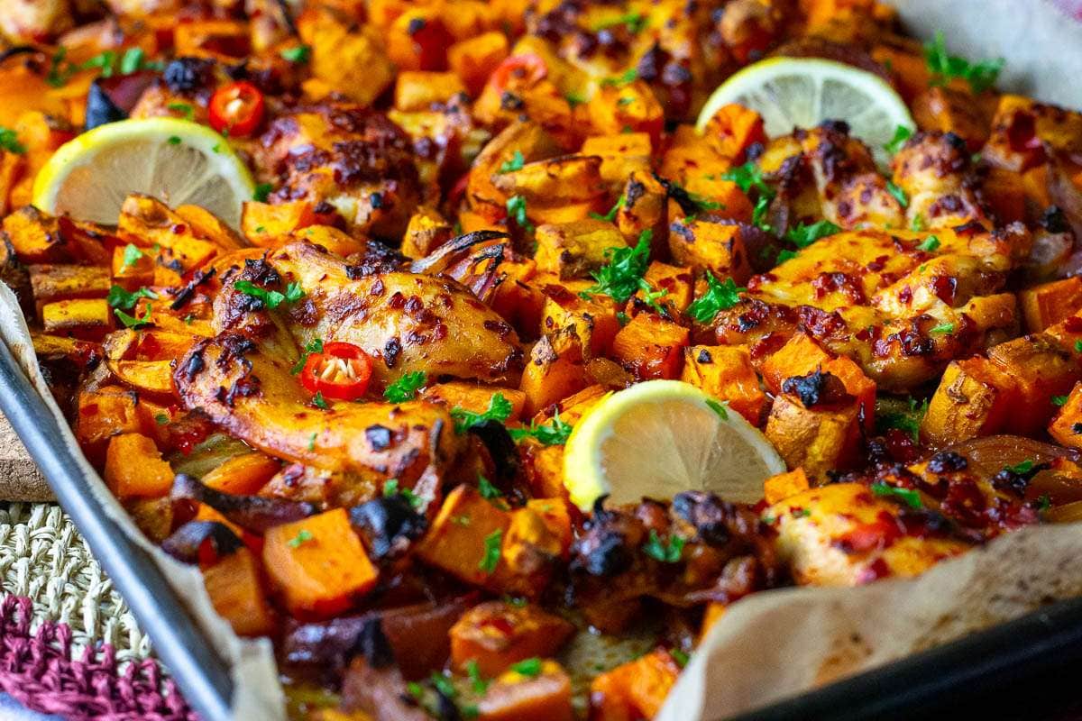 Harissa Chicken Thigh Tray bake after baking garnished with lemon slices.