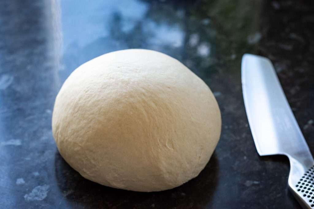 Sourodugh shaped into a tight ball on a dark work surface.