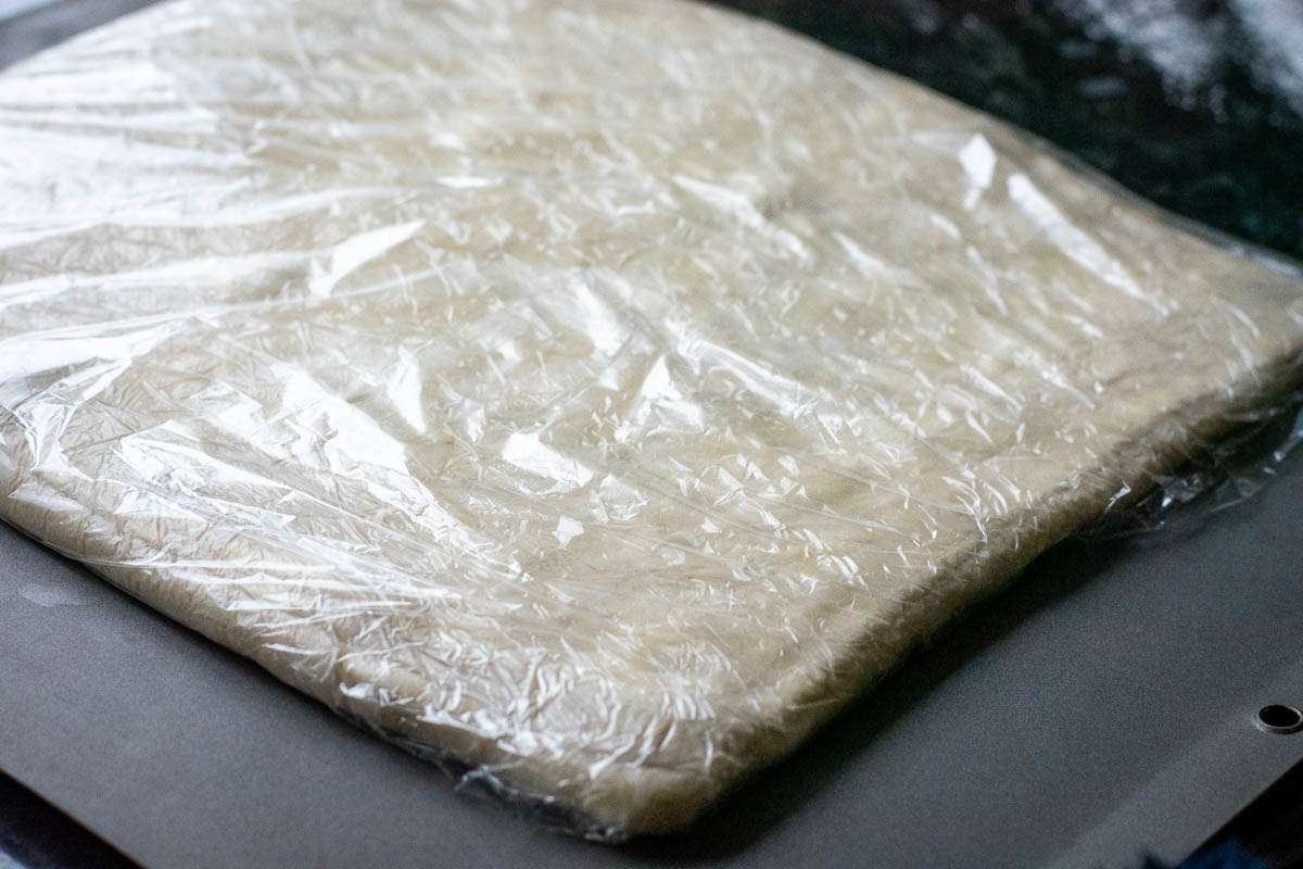 Laminated sourdough pastry rolled ou thinly, wrapped in plastic wrap and placed on a large baking sheet for chilling.