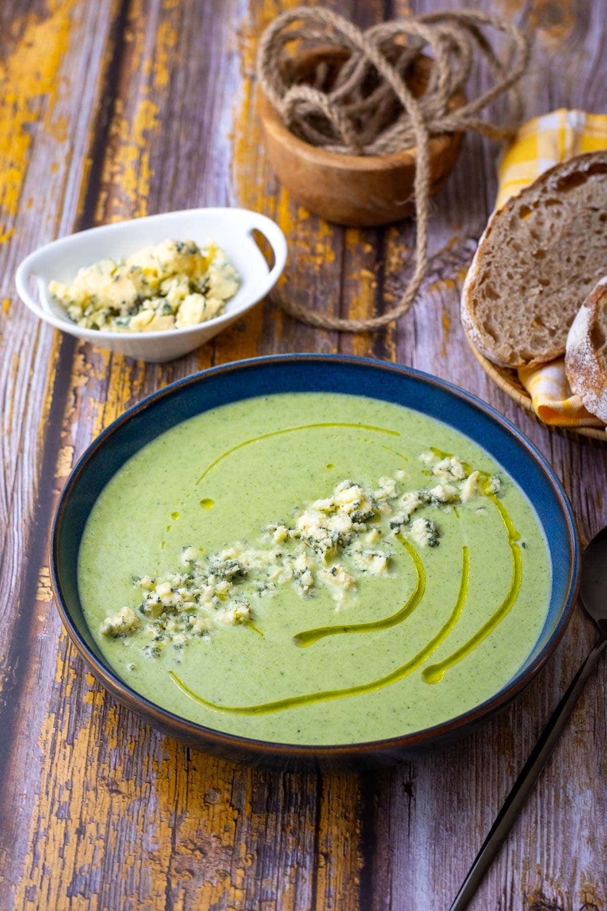 Broccoli and blue cheese soup in a blue bowl garnished with a drizzle of oil and crumbled stilton.