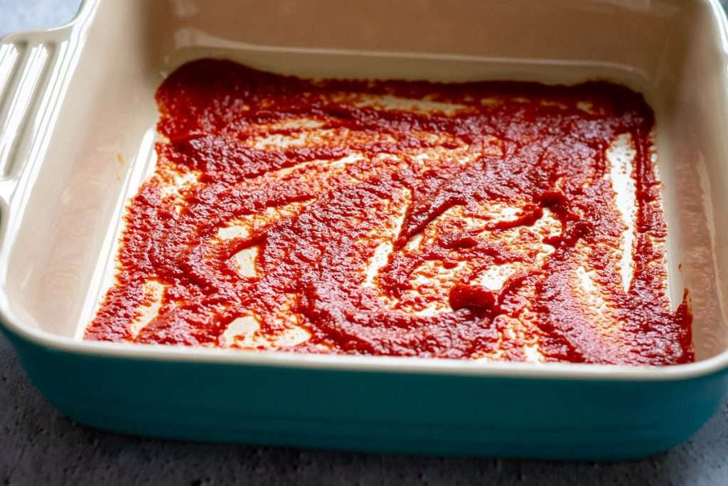 The first layer of tomato sauce in a casserole dish.