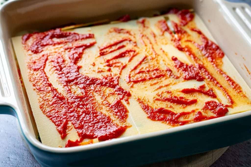 Spreading the remaining tomato sauce all over the lasagna sheets.