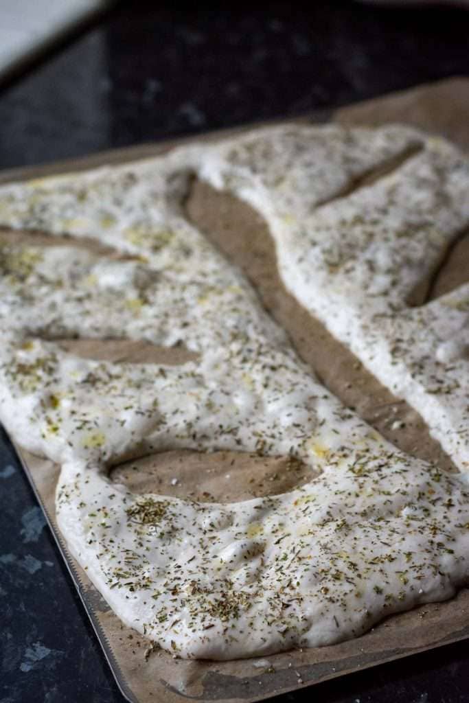 Sourdough fougasse shaped and sprinkled with herbs de provence and salt, ready to be baked.