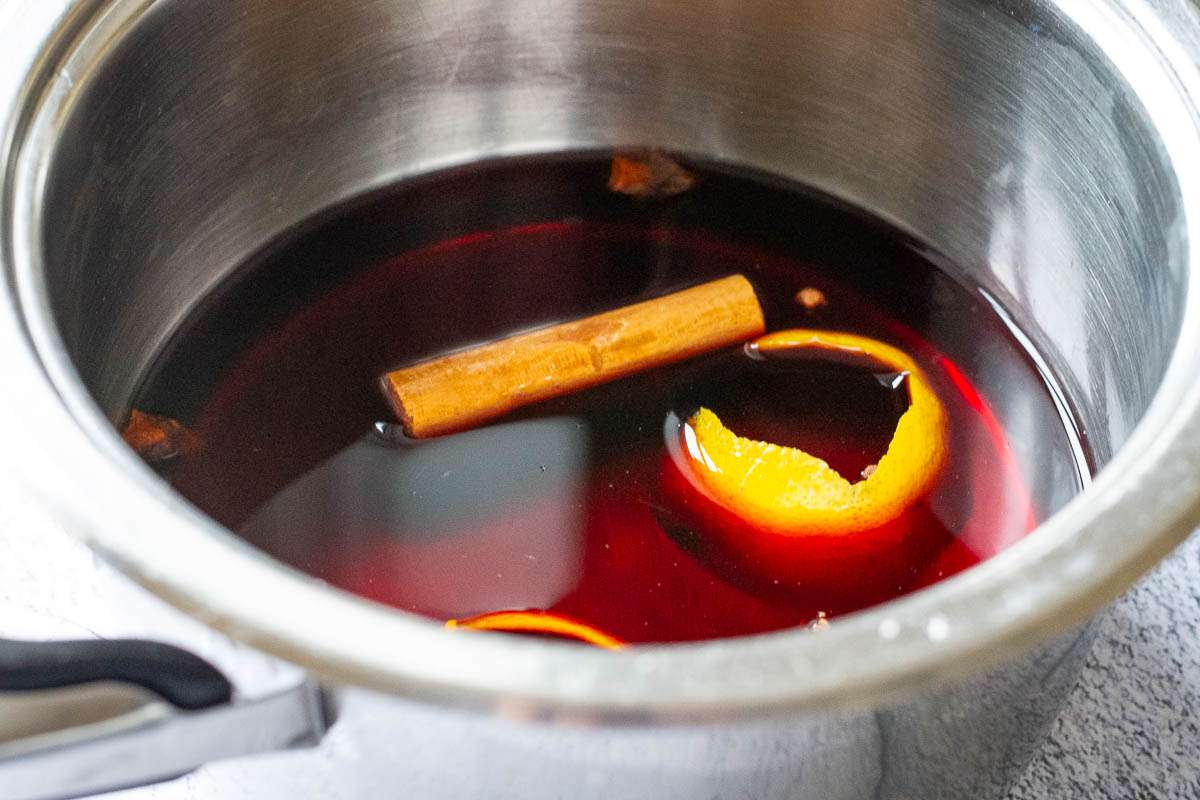 Lemon and orange zest, cloves, star anise and cinnamon stick floating in mulled wine in a pan.