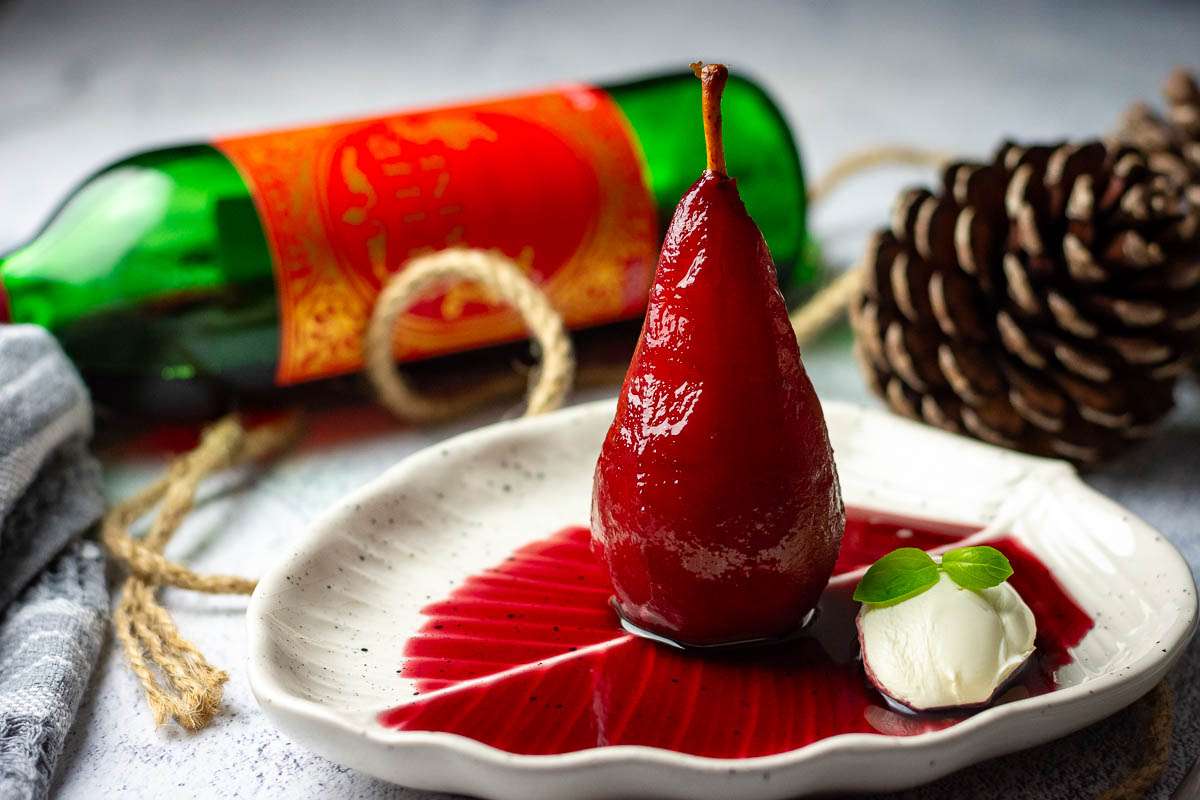 Burgundy red poached pear with mulled wine sauce and a dollop of creme fraiche on a white plate.
