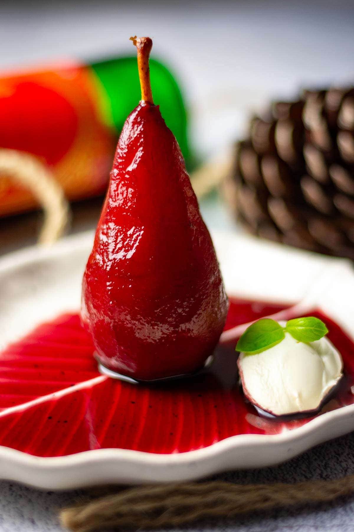 A mulled wine poched pear standing upright on a white leaf shaped plate.
