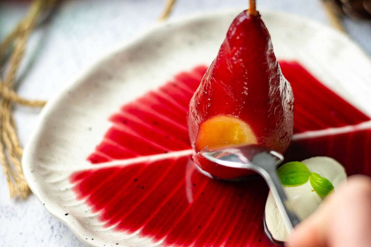 Taking a first spoonful of Mulled wine poached pear drenched in mulled wine sauce.