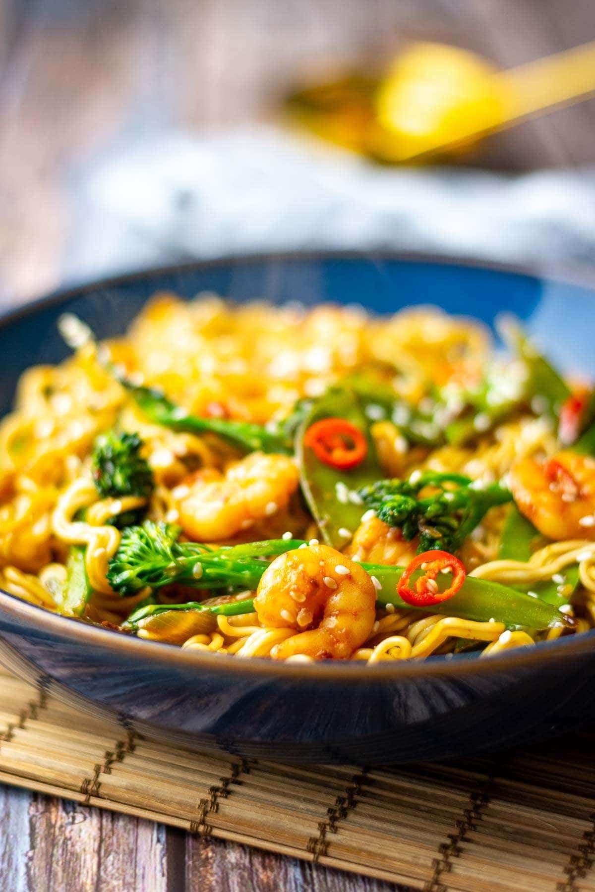 teriyaki prawn stir fry with noodles in a blue bown on a wooden table.