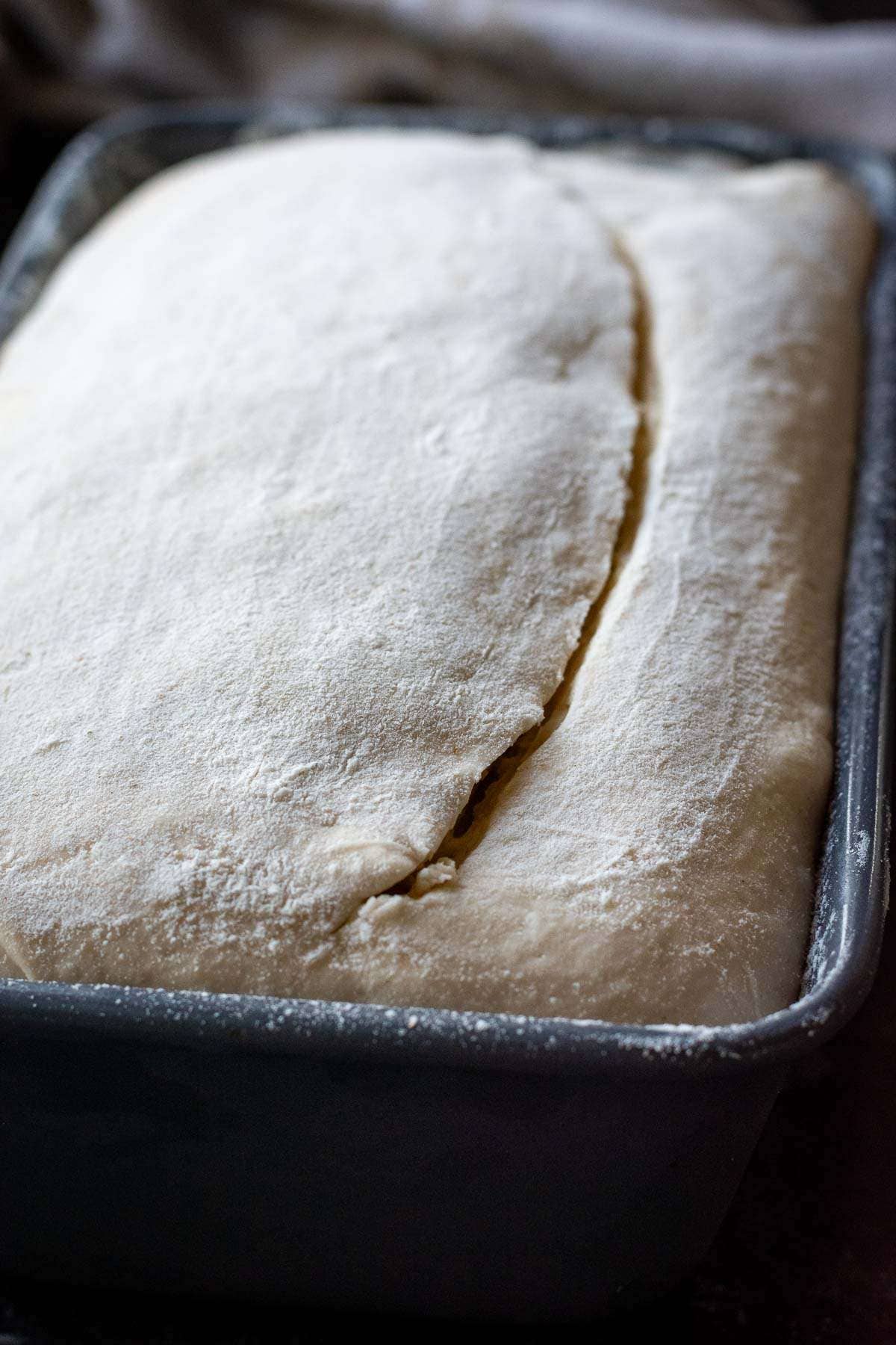 Scored sourdough bread in a loaf pan.