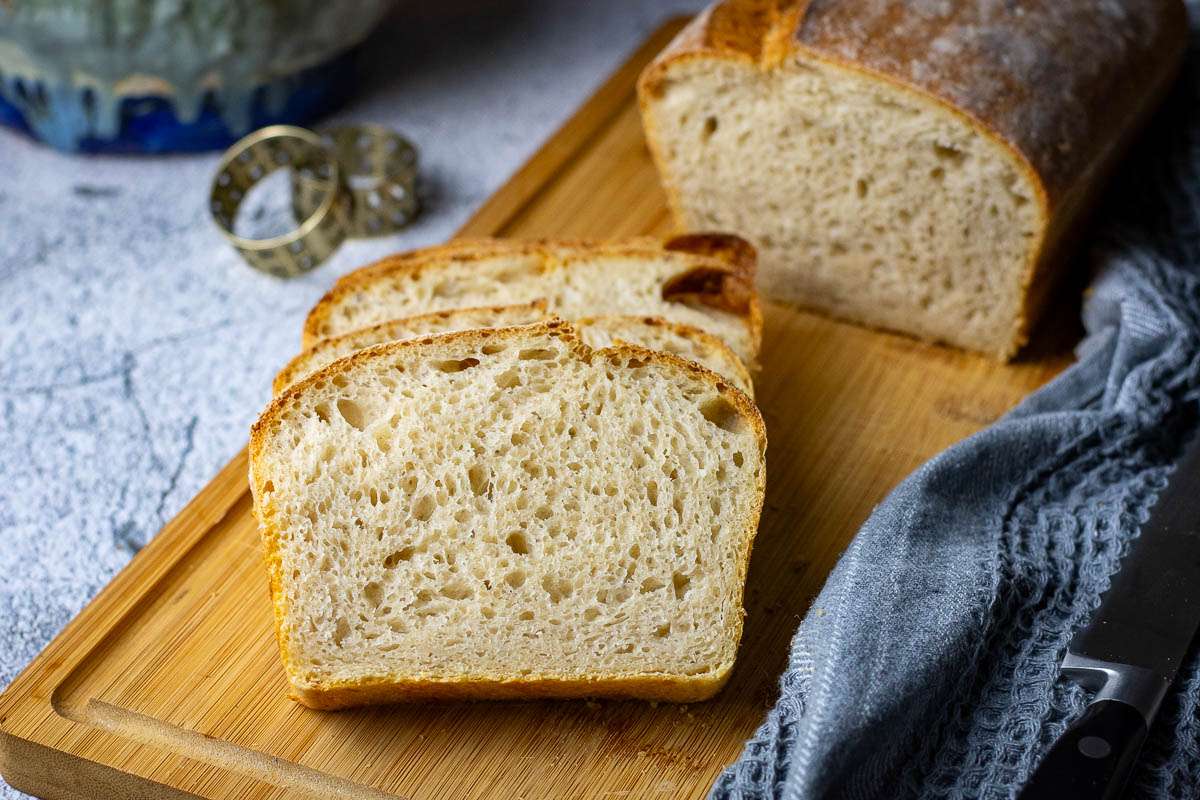 Sourdough baked in a loaf pan, sliced on a wooden board.