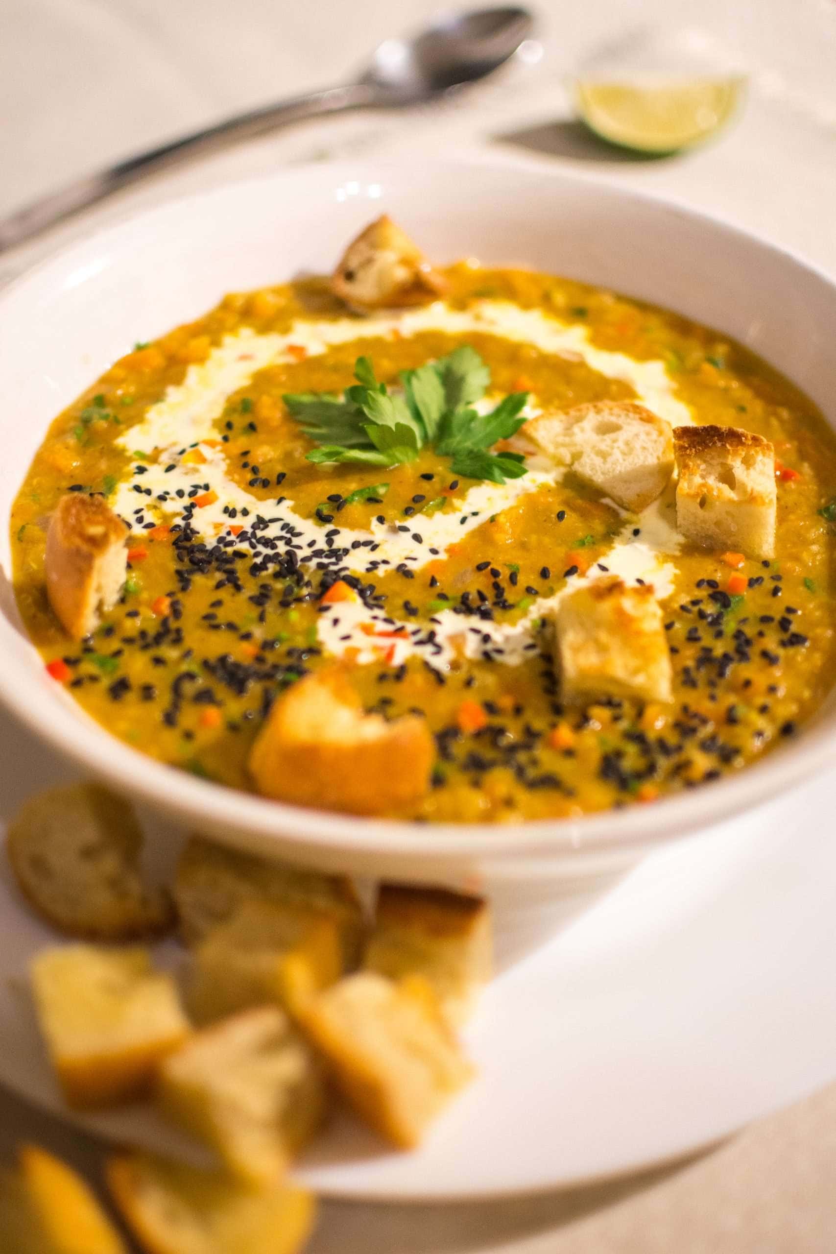 Carrot and lentil soup with nigela seeds and croutons on top.