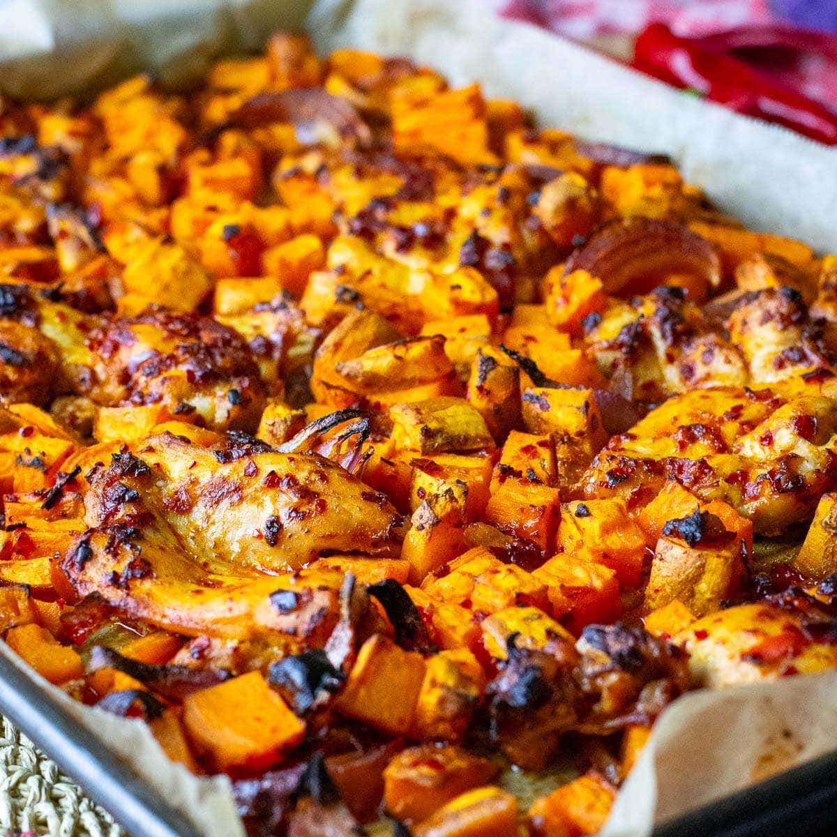 Baked Harissa Chicken Thighs on a large baking tary with sweet potatoes and red onion.