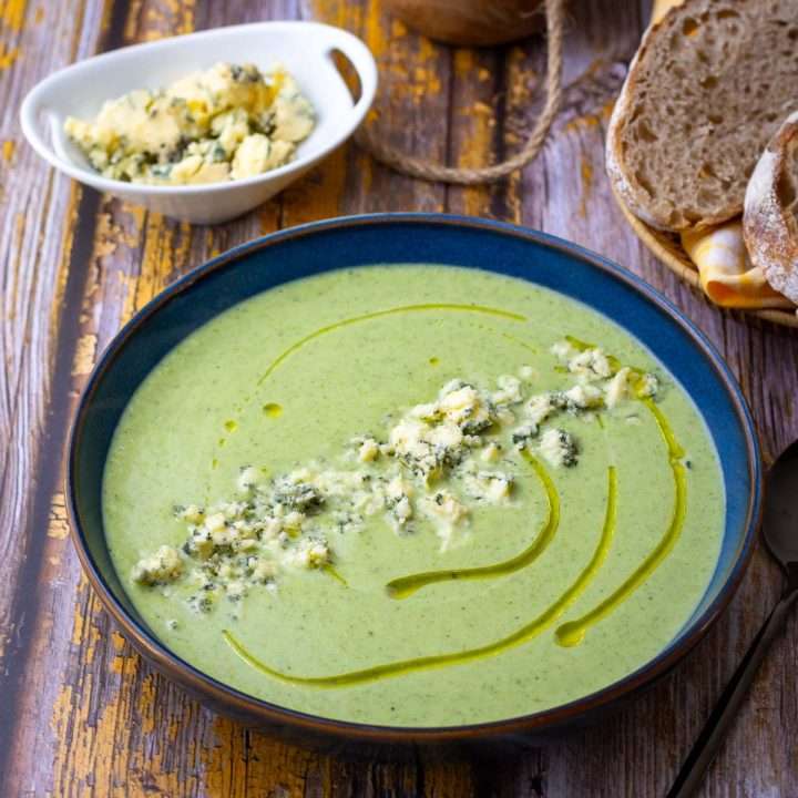 Broccoli and blue cheese soup in a blue bowl garnished with a drizzle of oil and crumbled stilton.