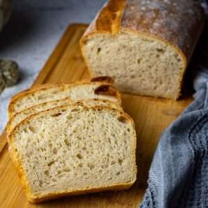 Sourdough baked in a loaf pan, sliced on a wooden board.