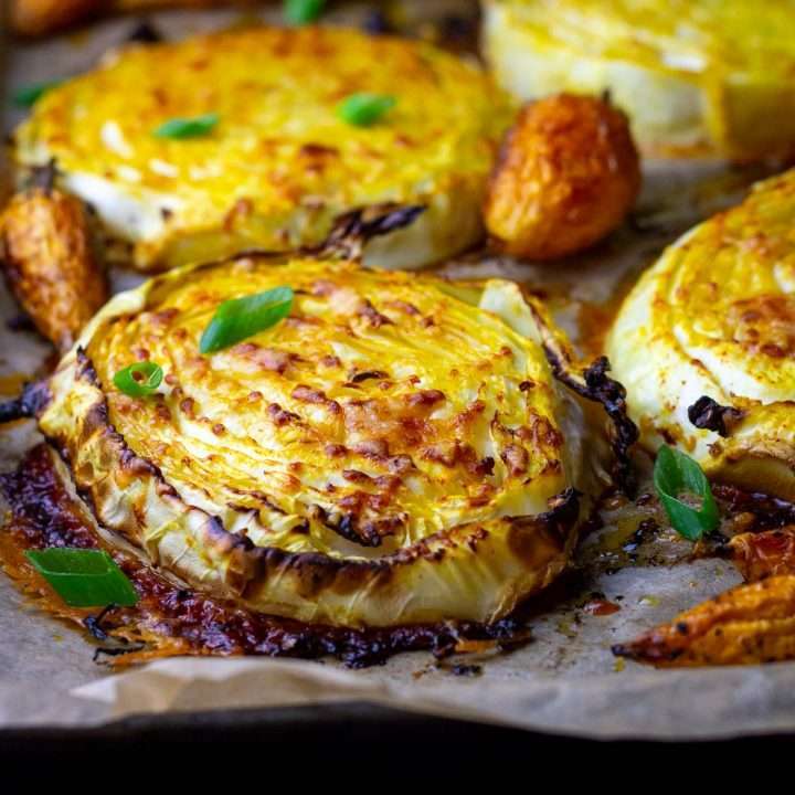 Four Roasted Cabbage Steaks With Parmesan on a baking tray lined with parchment paper.