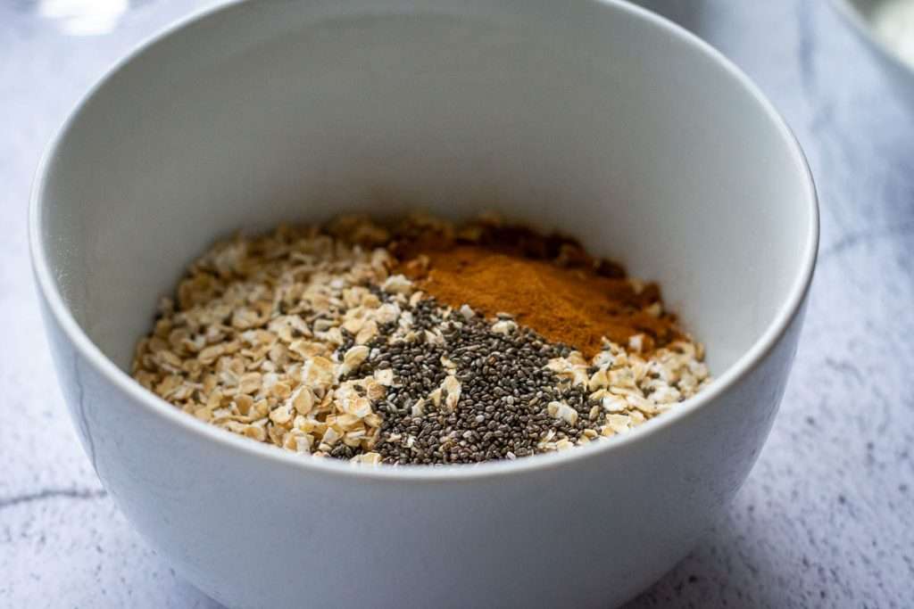 Oats, cinnamon and chia seeds in a small white bowl.