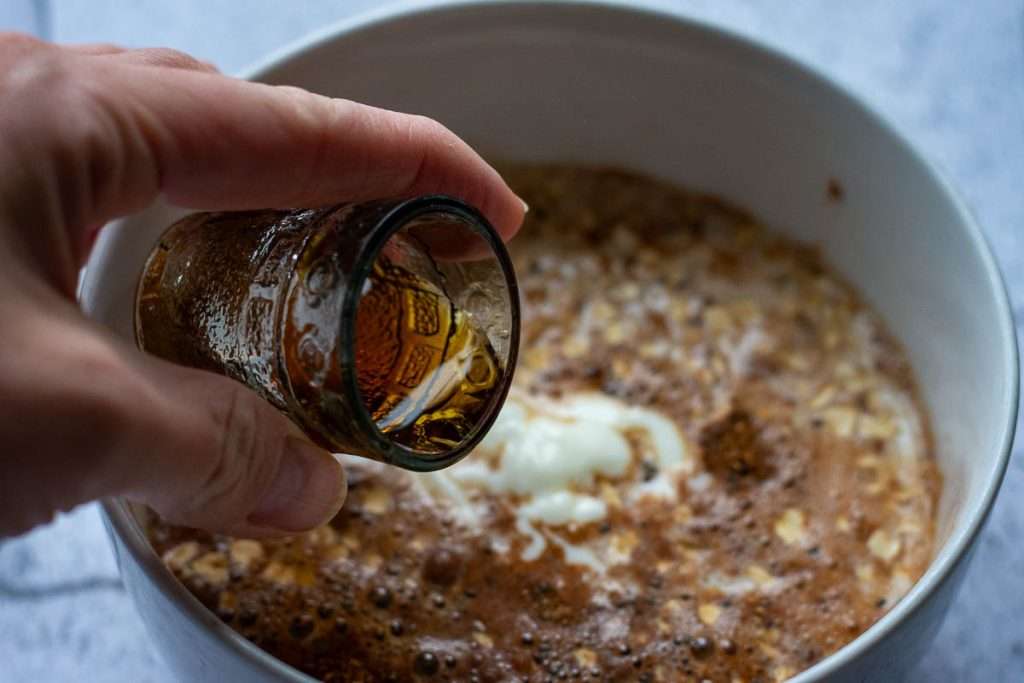 Adding maple syrup to the oats with milk and yogurt.