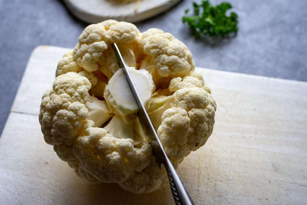 Cutting cauliflower head in half through the middle of the core.