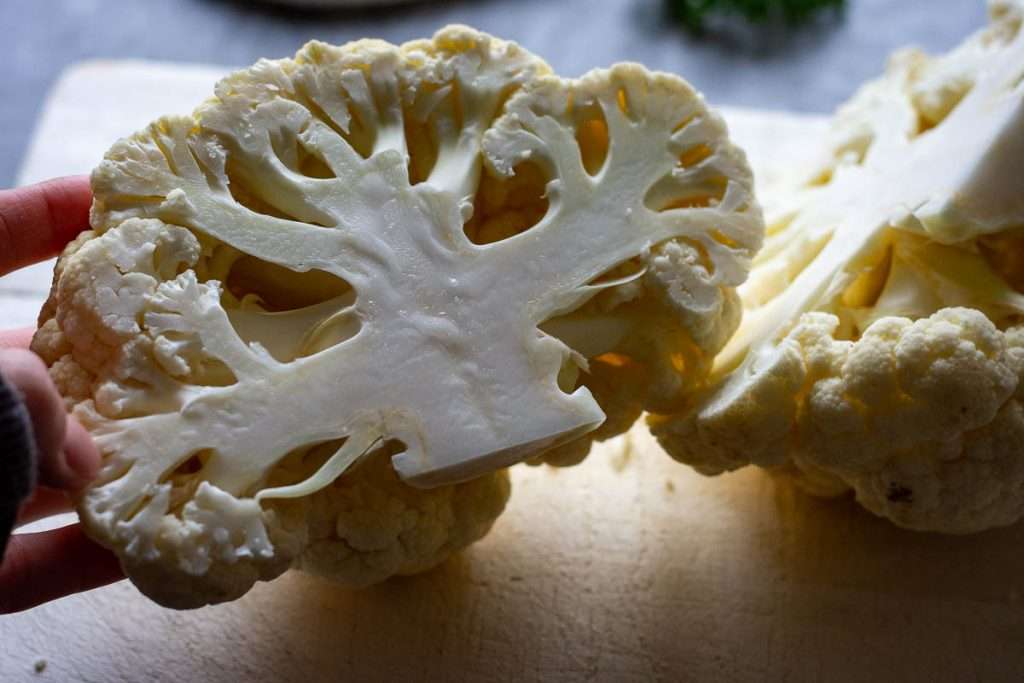 Cauliflower head half on a wooden board.