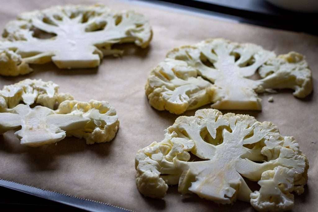 4 cauliflower steaks on a baking sheet lined with parchment paper.