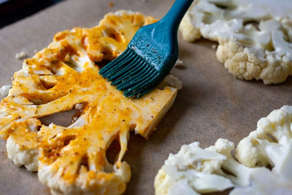 Brushing the spiced oil onto cauliflower steaks with a pastry brush.
