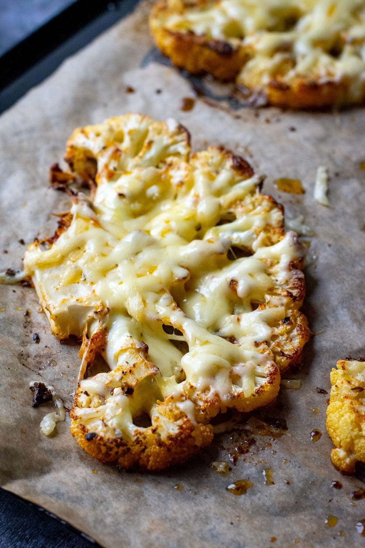 Cauliflower steak with cheese melted on top on a parchment paper lined baking sheet.