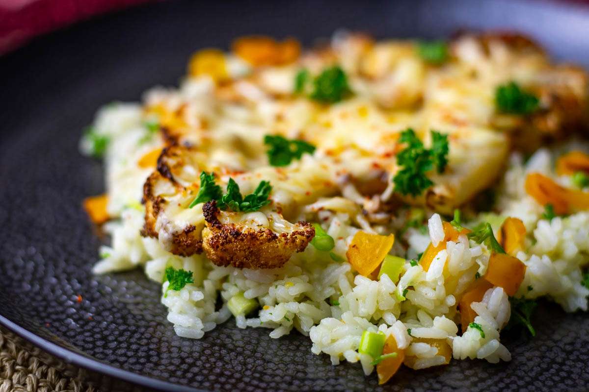 Cheesy Cauliflwoer steak on a black plte garnished with parsley.