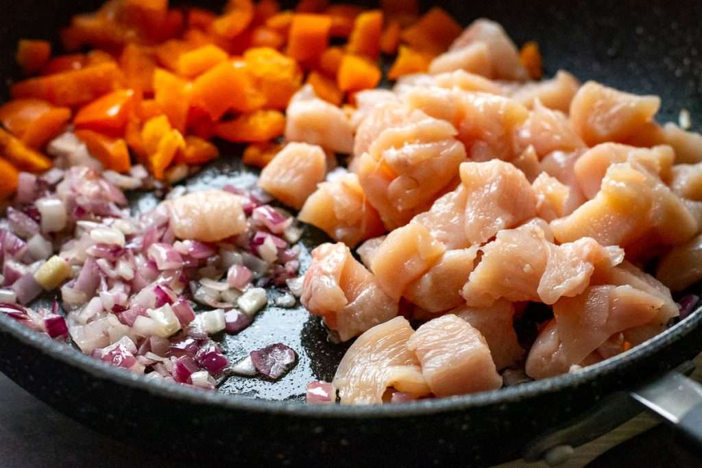 Chicken, bell pepeprs and onion in a frying pan.