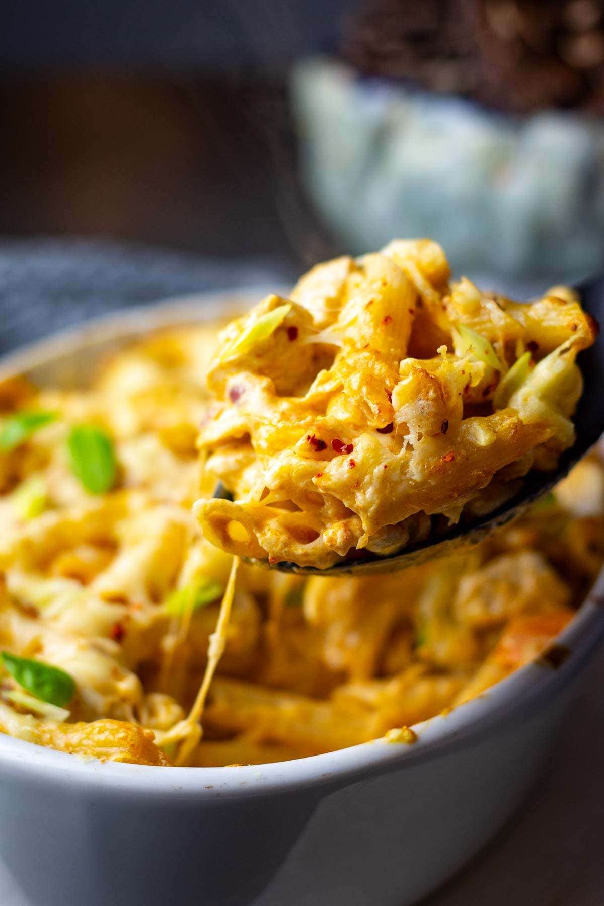 Strings of cheese pulling away from the chicken pesto pasta bake as a large spoonful is being served.