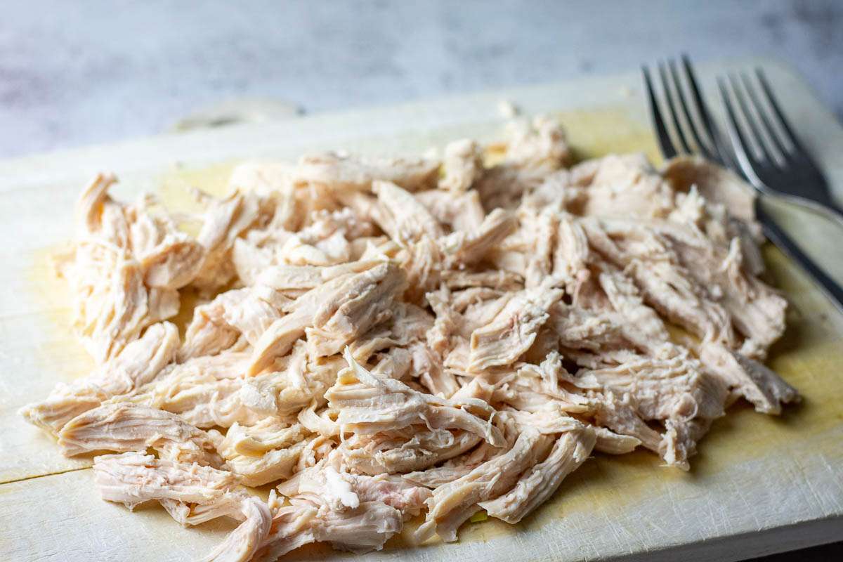 Poacjed chicken shredded to pieces on a wooden chopping board.