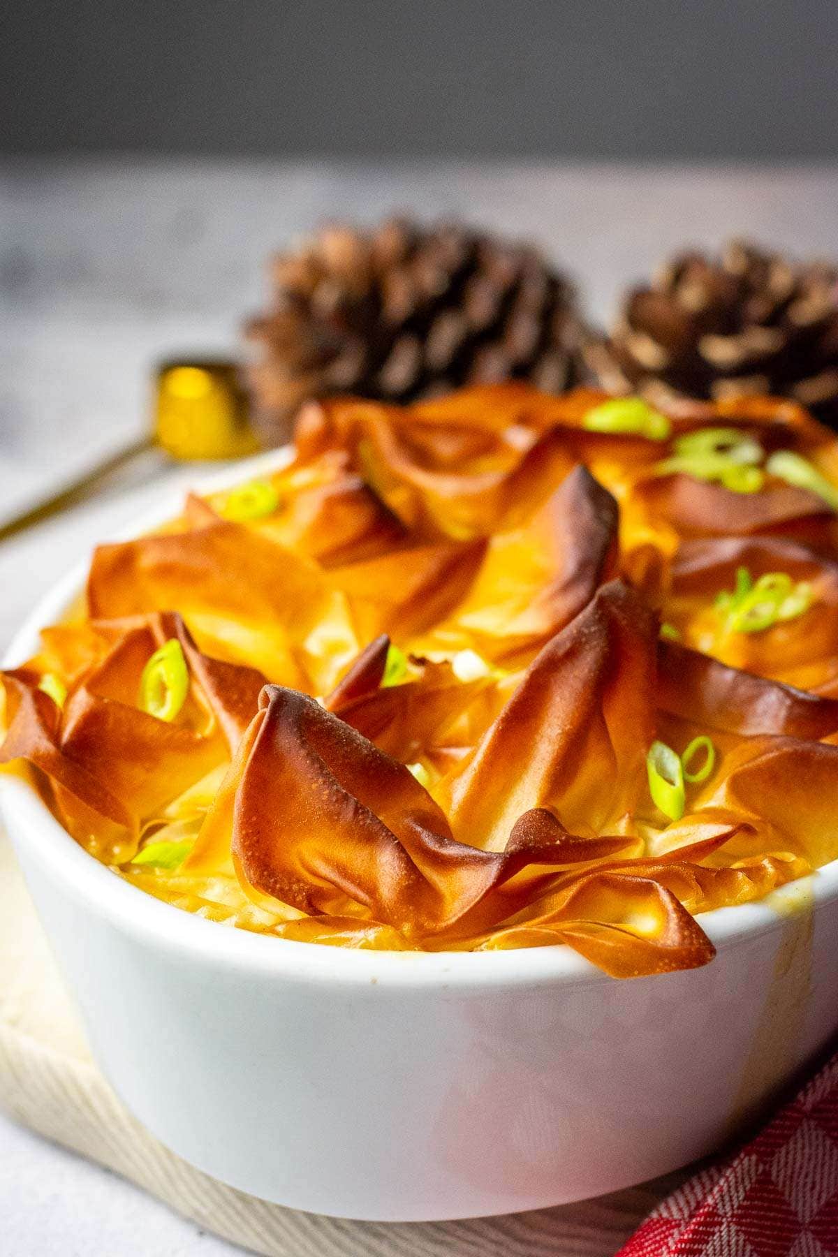 Scrunched up deep golden brown filo pastry top on a the chicken, bacon and leek pie in a white pie dish.
