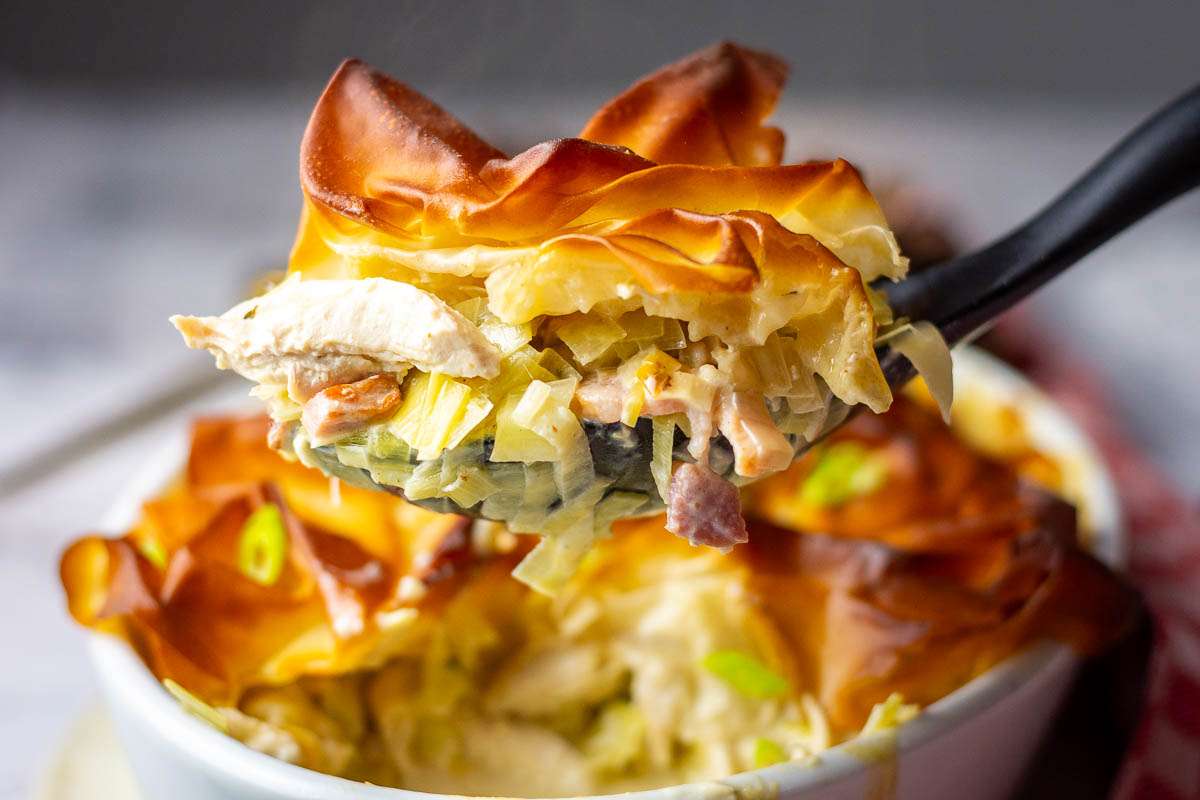 A portion of chicken, bacon and leek pie being lifted out of the white pie dish.