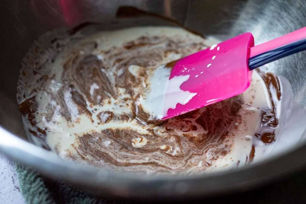 Mixing melted chocolate and cream with a pink rubber spatula.