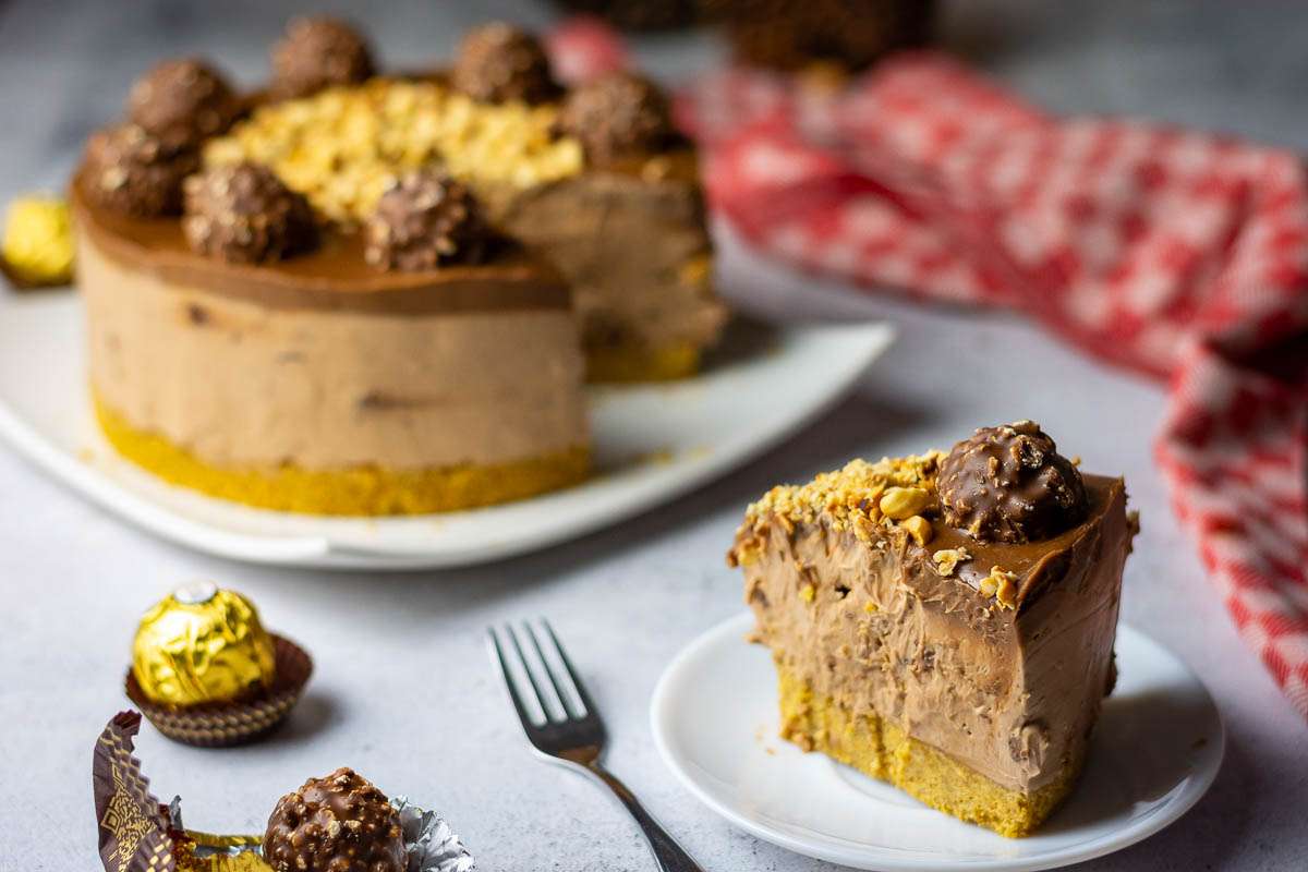 A slice of cheesecake with ferrero rocher on top on a white late.