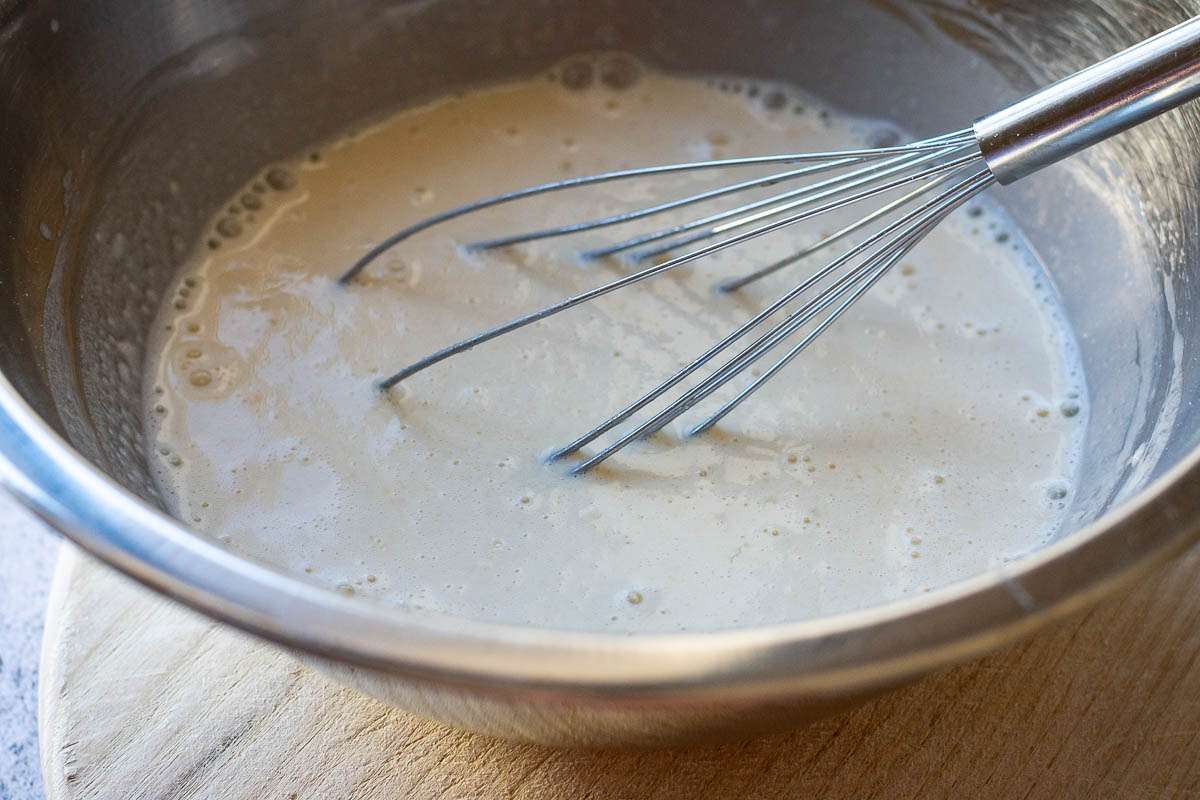 Crepe batter in a mixing bowl with a balloon whisk in it.
