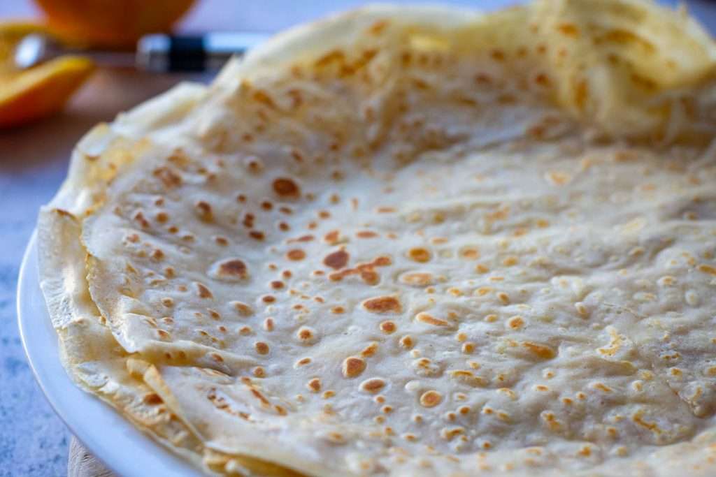 Homemade crepes piled on a white plate.