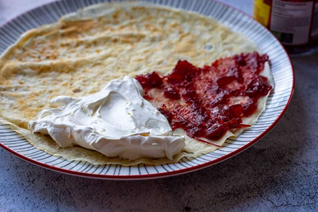 Orange cream spread on one quarter of the crepe, and cranberry sauce spread on another quarter before folding.