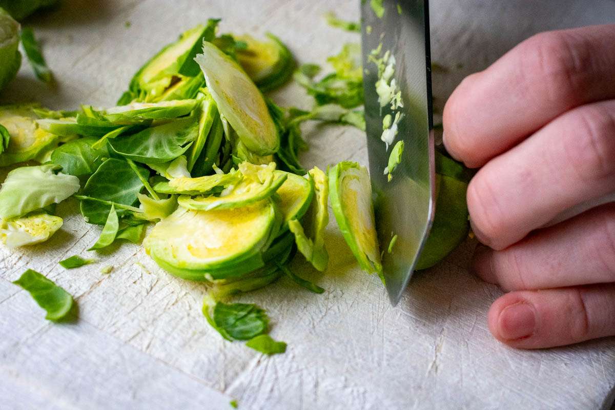 Cutting Brussels sprouts thinly using a sharp knife on a wooden chopping board.