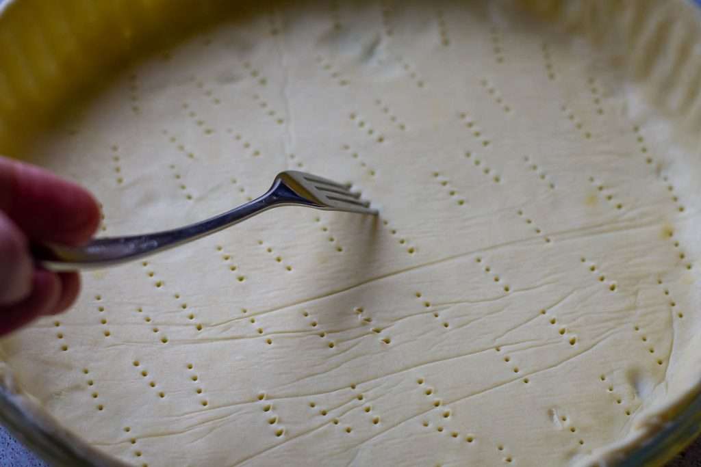 Pricking the base of the shortcrust pastry with a fork.