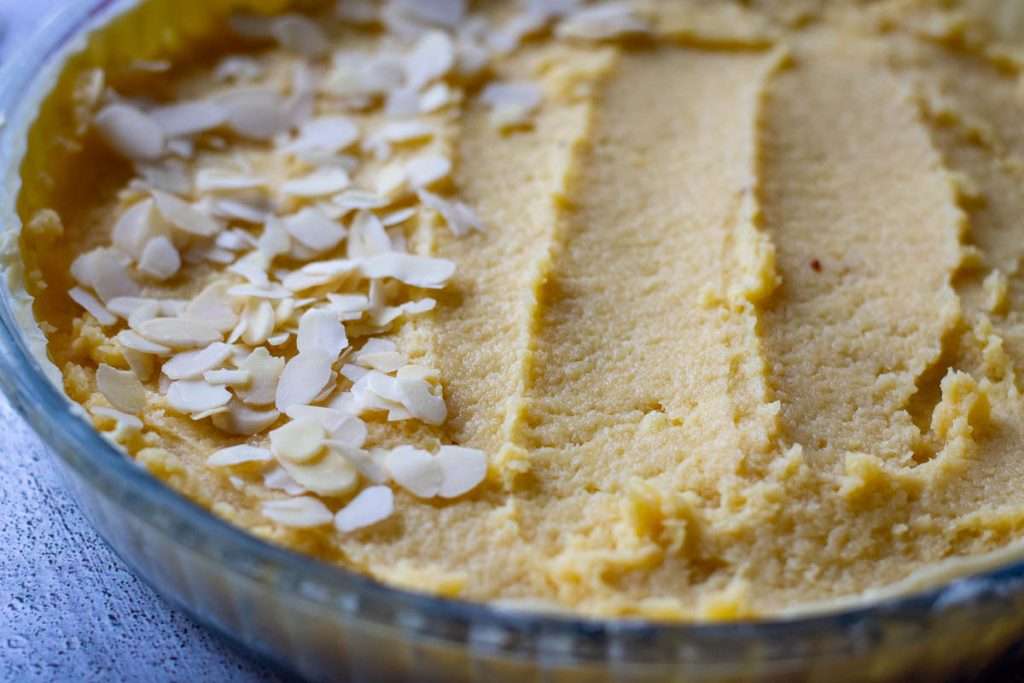 Frangipane filling spread in an even layer with half of it already covered with flaked almonds.