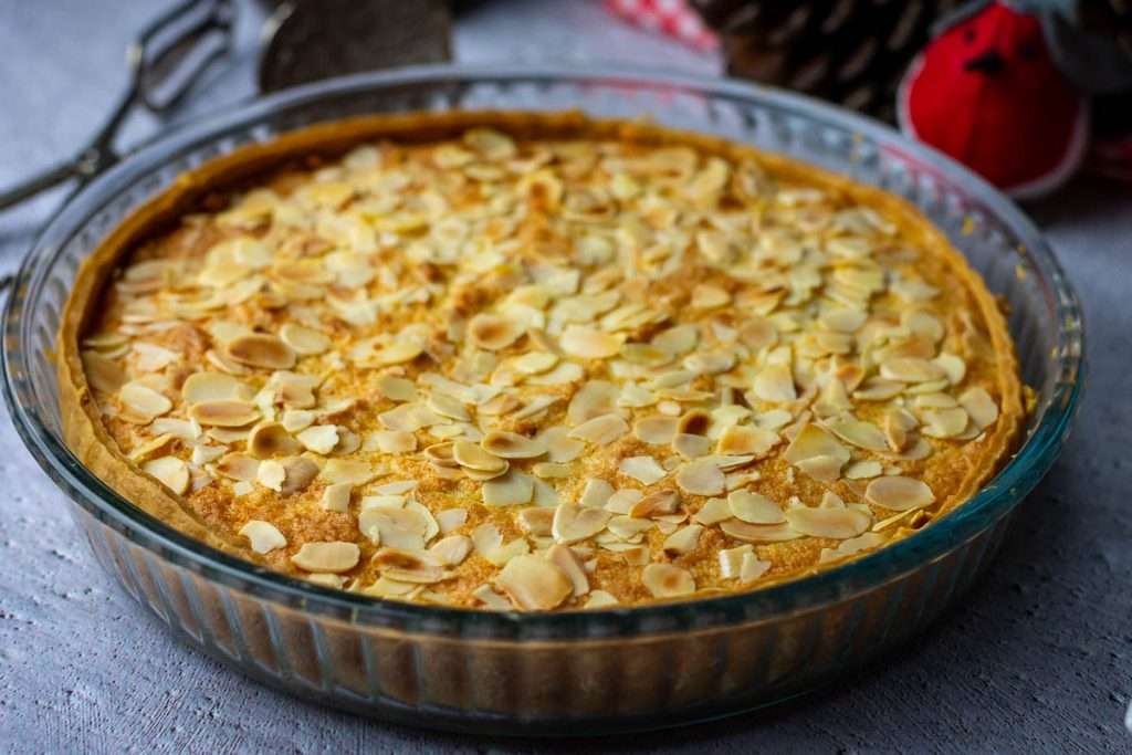 Baked, golden brown Mincemat Bakewell Tart on a grey surface.