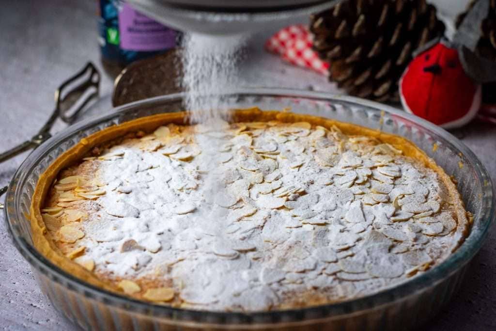 Dusting the Christmas bakewell tart with icing sugar.