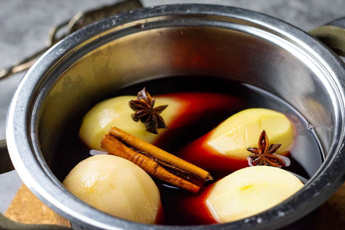 Four peeled pears lowered into the port and spice mixture.