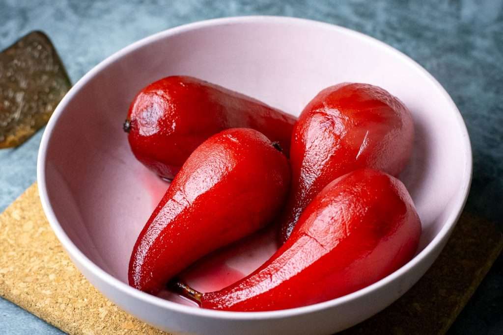 Port poached pears resting in a pale pink bowl whilst the syrup is being reduced.