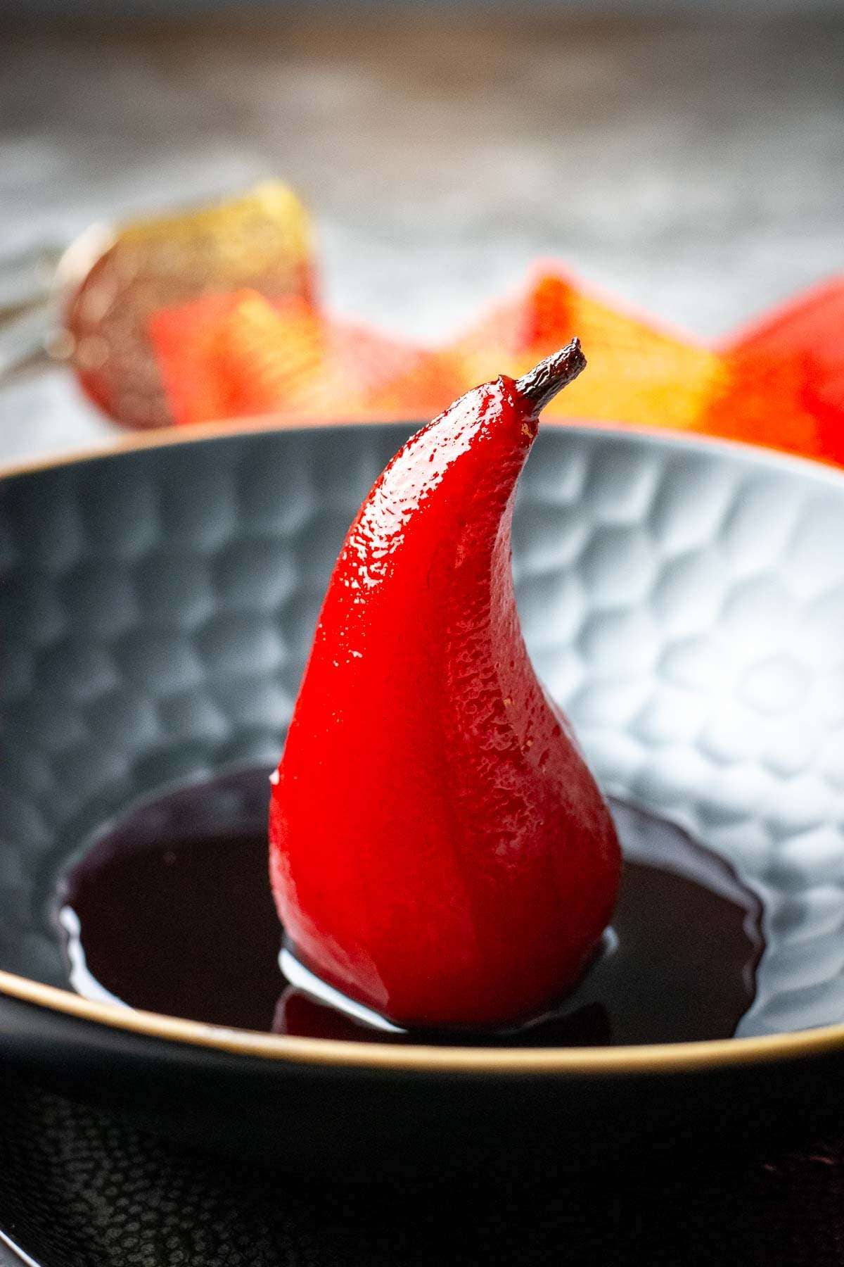 Pear poached in port wine standing proudly in a small pool of port syrup in a black bowl.