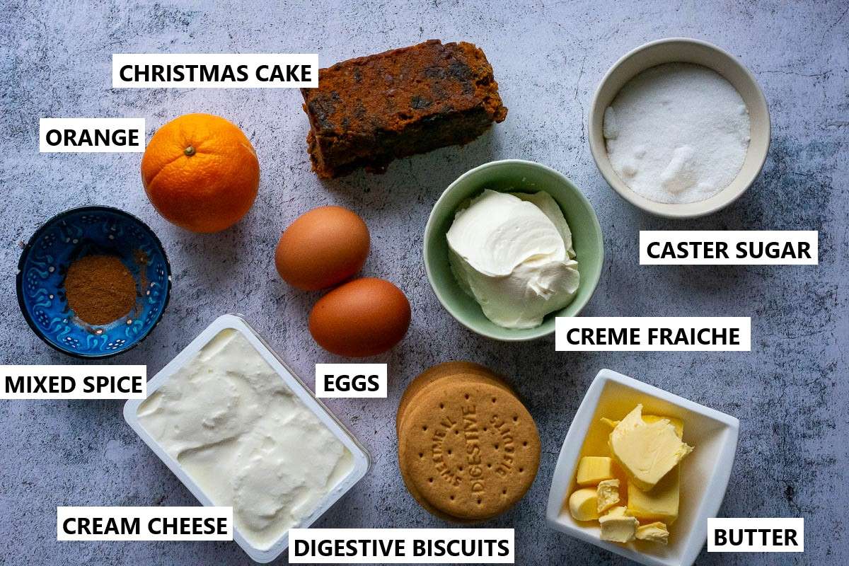 Ingredients for Christmas cheesecake with Christmas cake on a light grey surface.