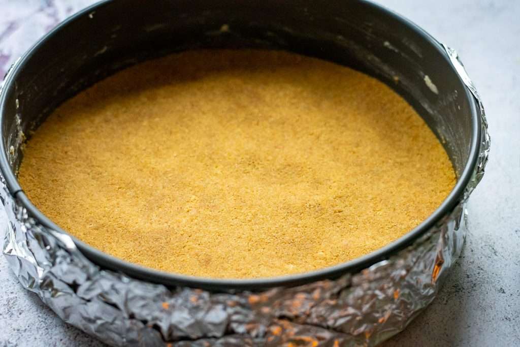 Buttery biscuit crumb pressed into the base of the cake tin.