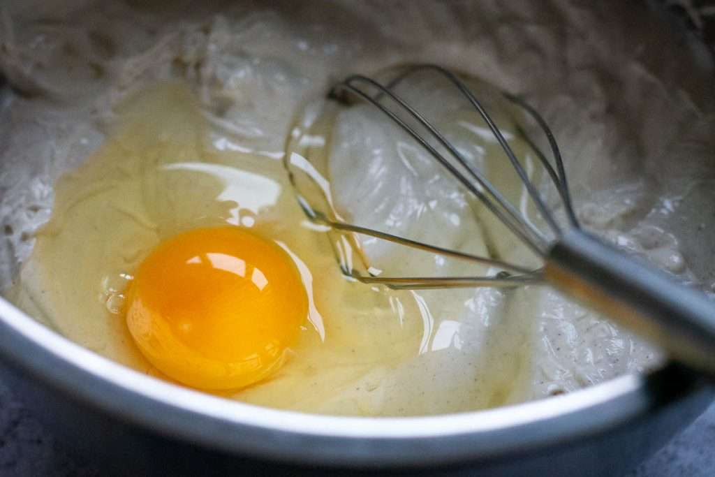An egg added to the Christmas cheesecake mixture, with a balloon whisk in it.
